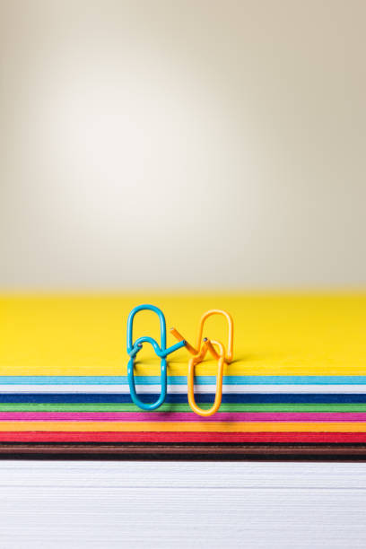 istock Two paper clips appear to be having a relaxed conversation sitting on a multicolored sheet. 1477205573