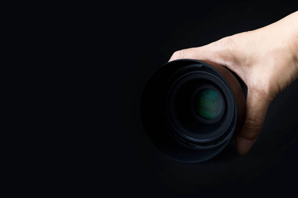 istock Camera lens in hand holding isolated on black background. copy space 1477209518