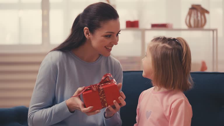 Little girl runs to her mom, presenting a red gift box, celebrating Mother's Day