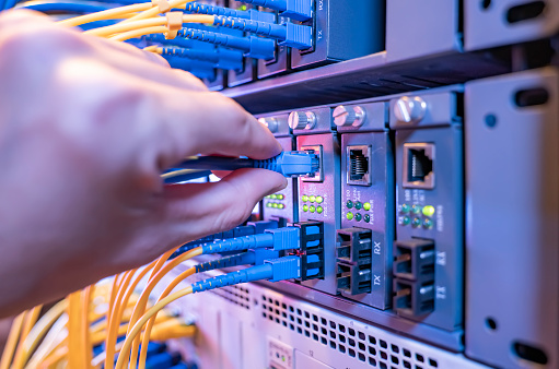 man working in network server room with Fiber Optic cables connected to optic ports and UTP