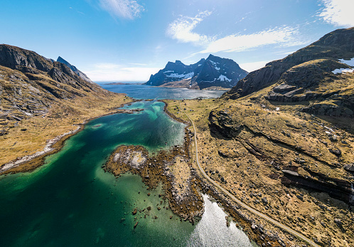 Aerial drone view of Vindstad village in Lofoten, Norway, small colored houses, big mountains and a bluish lake, during spring on a clear day