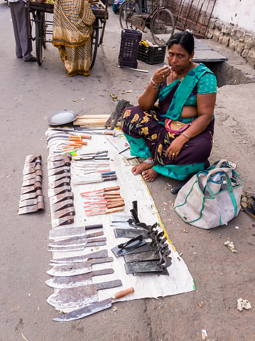 Warangal, Telangana, India - March 2019: An Indian woman selling knives on the street at her roadside shop in the market.