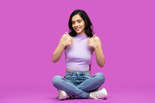 Photo of young happy pretty girl holding thumbs up on purple background