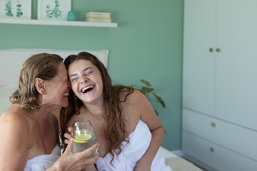 Argentinean 74 years-old grandmother and 18 years-old granddaughter drinking lemonade and having fun during a spa day at home. Senior woman has rosacea and young woman vitiligo, so they take care their skin. Buenos Aires - Argentina
