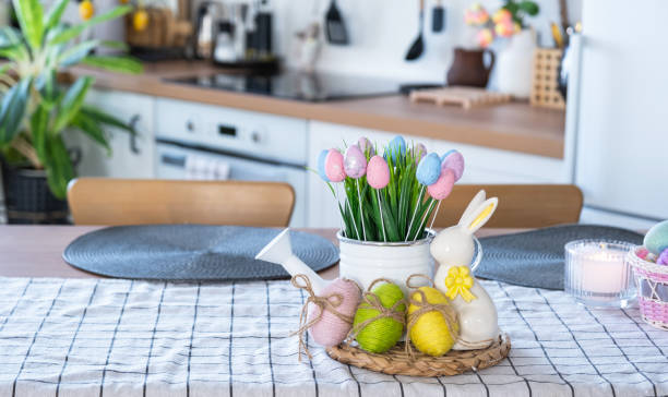 istock Easter decoration of colorful eggs in a basket and a rabbit on the kitchen table in a rustic style. Festive interior of a country house 1477217184