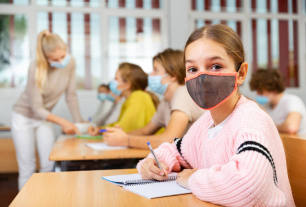 istock Schoolgirl in mask sitting in classroom 1477219615