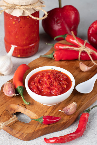 Traditional sauce adjika with hot chili pepper, paste harissa in white bowl on wooden board, Vertical format