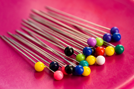 Sewing Pins in a Row - Colorful pin needles used for sewing in colorful vibrant pink magnetic plastic tray closeup detail.