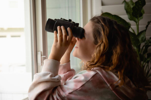 istock Girl looking out window with binoculars 1477227097
