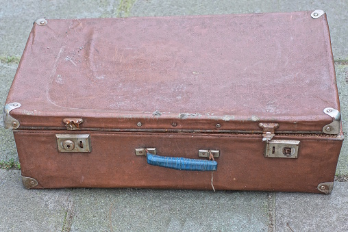 one large closed brown old leather suitcase lies on gray asphalt in the street