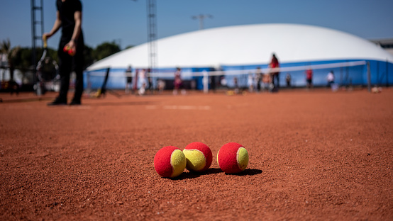 tree red tennis balls are on clay court focus on foreground players are background horizontal still