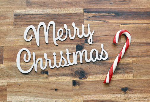 Closeup of mass produced, generic lettering spelling out Merry Christmas next to a giant candy cane on a wood background.