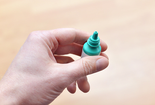 Closeup of a man's hand holding generic, mass produced eye drops.