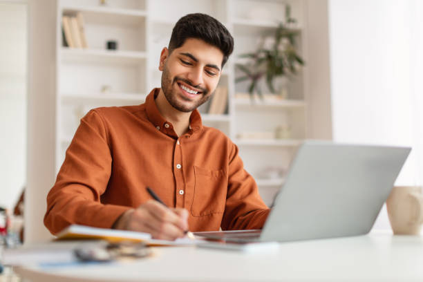 istock Portrait of smiling Arab man using laptop and writing 1477233967