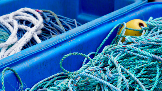 Nautical background with two bright blue plastic containers filled with tangled green, blue and white ropes and one yellow float on a quayside in Devon