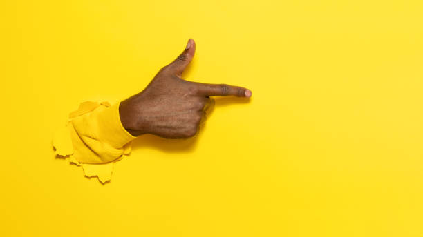 istock African american male hand pointing aside on virtual object or text, gesturing through the torn yellow paper background 1477239588