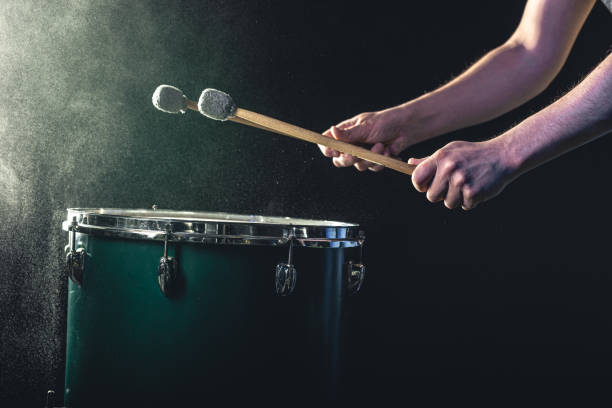 un uomo suona uno strumento a percussione musicale con bastoncini su uno sfondo scuro. - samba dancing dancing drum drumstick foto e immagini stock