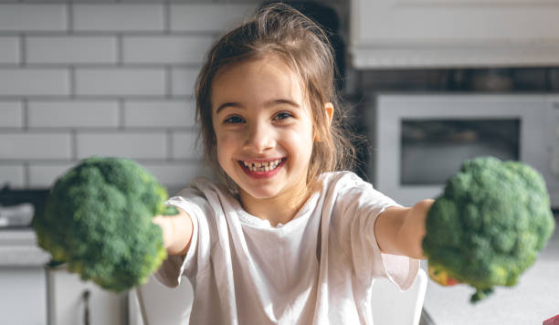 Funny little girl with broccoli in the kitchen. stock photo