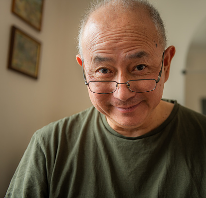 A kind, happy elderly Asian man at home with a smiling facial expression.
