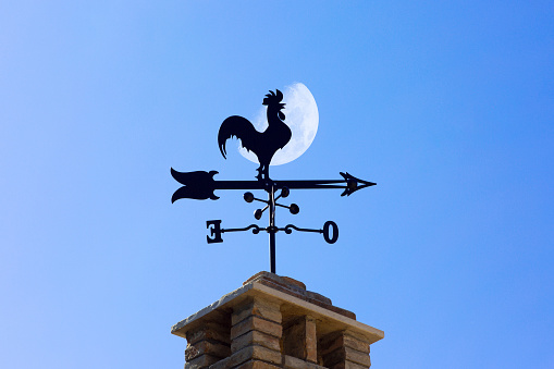 Black metal frame with a direction arrow, weathercock and east and ovest directions on a roof in the Chianti Classico Gallo Nero region.