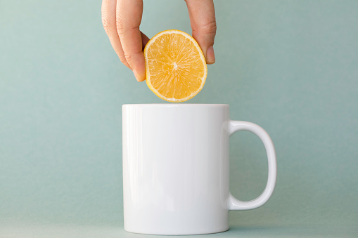 Hand Squeezing Lemon into tea cup, green background.