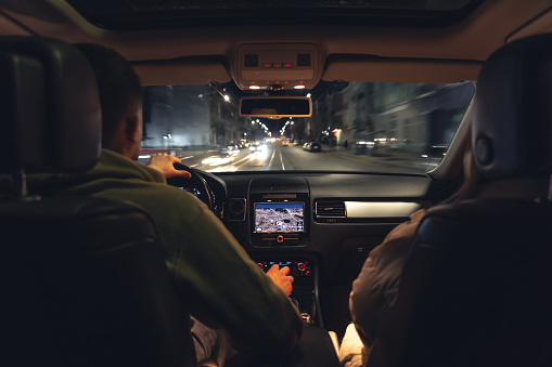A man and a woman are driving in a car at night, the view from the car to the road.