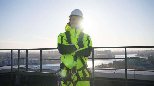 Portrait of a male industrial climber in work overalls folds his arms and looks at the camera smiling against the backdrop of the sun