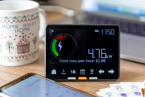 A rising home energy cost concept with a smart meter, bank notes, calculator and tea mug.