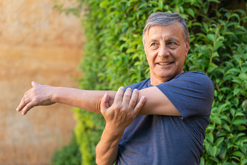 Senior man stretching arms while outdoor exercising