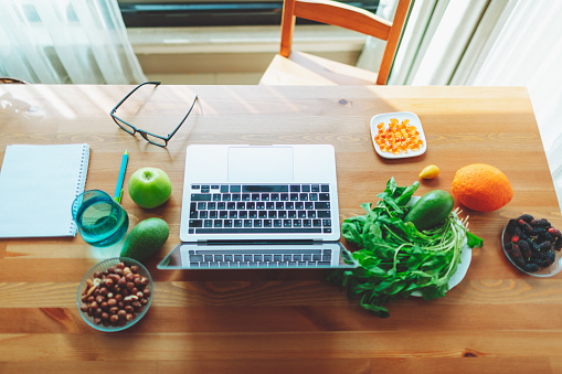 Nutritionist working place with laptop, eyeglasses, fruits, vegetables, nuts and greens
