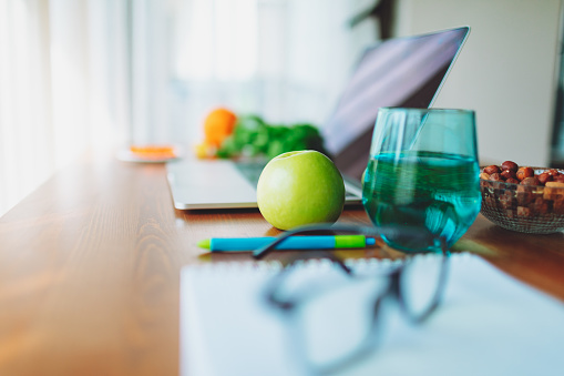 Nutritionist working place with laptop, eyeglasses, fruits, vegetables, nuts and greens