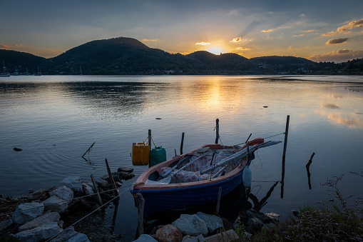 A old wooden boat on a sea bay with calm waters with the sun rising over the hill top. Lefkada island, Greece.