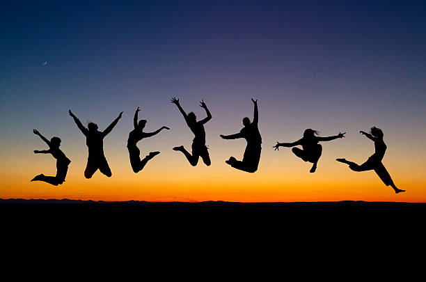 Silhouettes of seven people jumping against sunset  stock photo