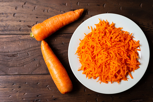 High angle view of  healthy  organic carrot grated in a white plate over a rustic wood table.