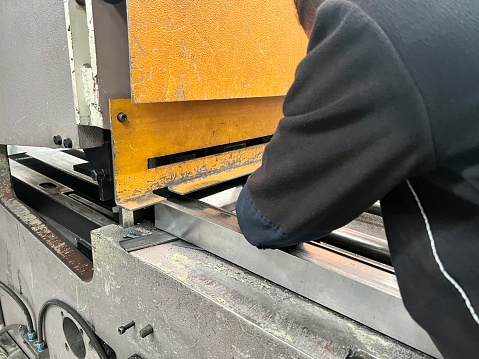 worker cutting sheet metal on a sheet metal cutting guillotine