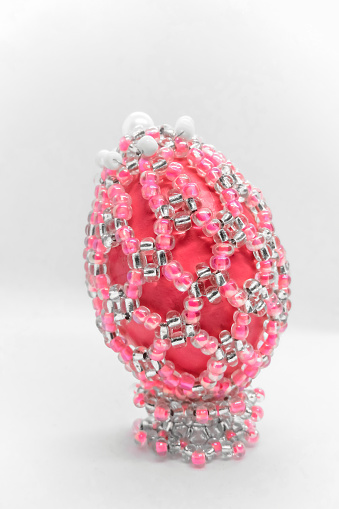 Pink beaded Easter egg on a light background. Easter holiday concept. Pink Easter egg decorated with beads on white background close-up