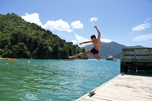 A boy jumps from jetty into the sea in summer. Taken in the Marlborough Sounds of New Zealand's South Island.