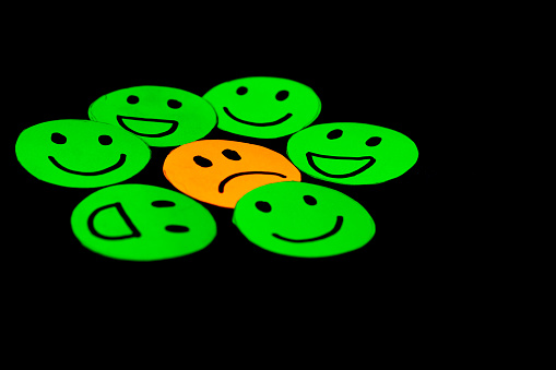 paper cutout image of green smiley faces surrounding a sad face. concept of psychology, therapy, emotions, mental health, circles of trust, friendship and family. Black background. Selective focus