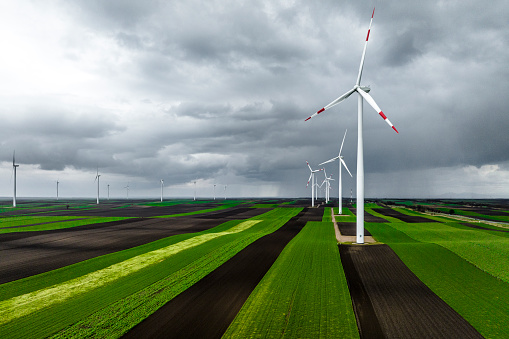 Windmills seen on the green and brown fields from a drone perspective during one stormy spring day.