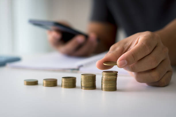 istock Businessman saving money concept financial. hand holding coins putting on stack using smartphone and calculator to calculate. concept of saving money for finance accounting. 1477266224