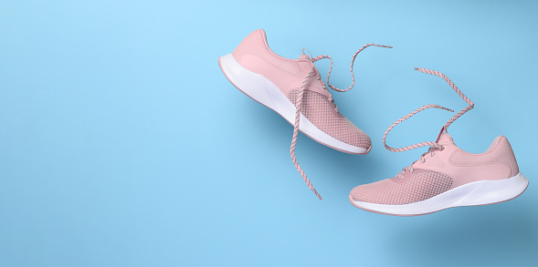 Pink women's sports sneakers with laces levitate on a blue background. Copy space