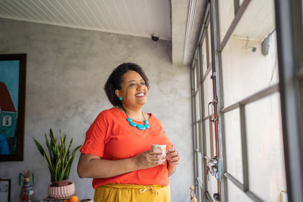 Black mature woman near the window drinking tea stock photo
