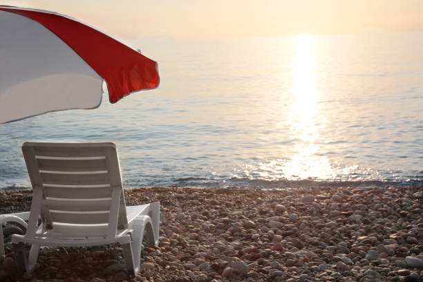 Empty sunbed and umbrella on stone beach near sea at sunset
