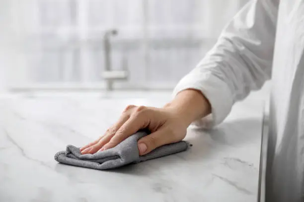 Woman wiping white marble table indoors, closeup