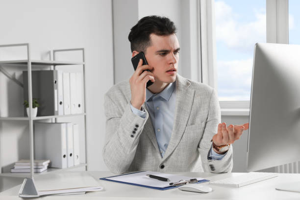 istock Confused businessman talking on phone while working in office 1477283275
