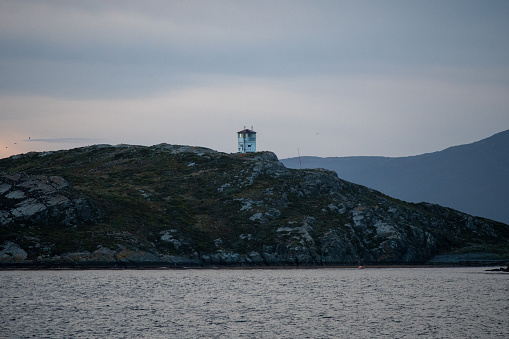 A lone watch tower stands perched on a rocky islands overlooking a bay at sunet.