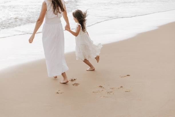 istock Happy kid with mother holding hands and strolling on sandy seashore 1477291521