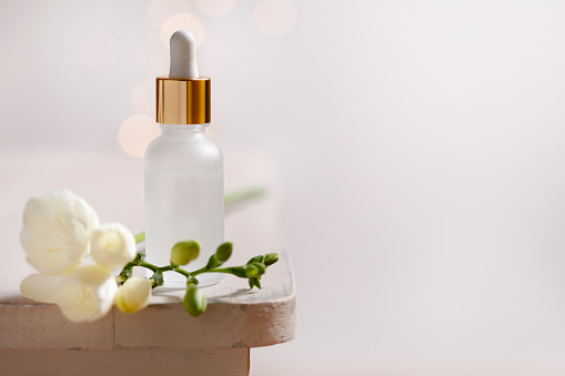 White and gold face serum bottle and white flower on rustic table with copy space