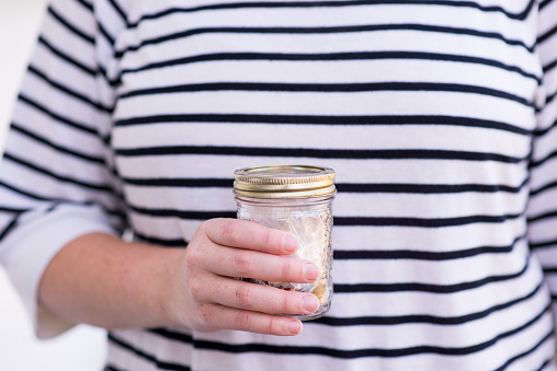 Anonymous woman is living a zero waste or low waste lifestyle by collecting the small amount of trash she makes over the years in a small glass jar. This makes a positive impact on the environment and the earth by not throwing out so much plastic to landfills.