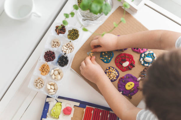 istock Baby boy creating plasticine diy figure with decorate dried beans element early development top view 1477297366